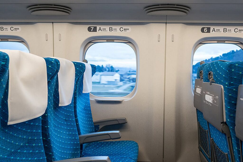 【富士山新幹線】青い座席が並ぶ新幹線の車内から窓の外の家と山並みが見える景色