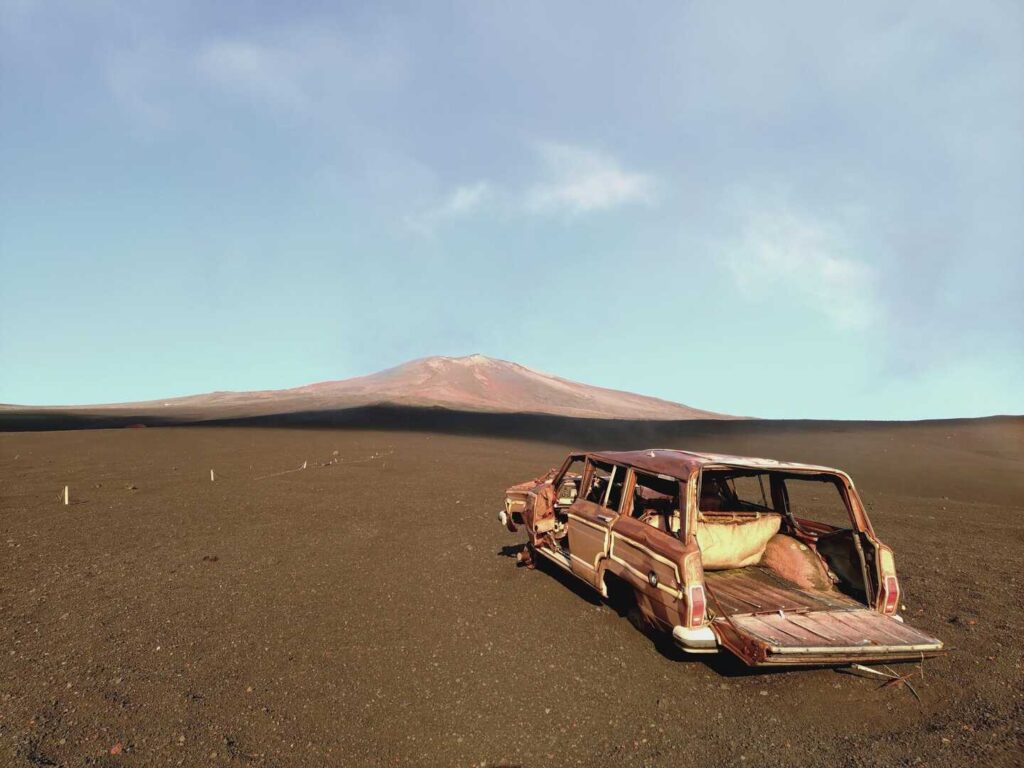 【富士山 ワゴニア 撤去】富士山を背景にした広大な黒い土の場所に窓が壊れて錆びた古いワゴニアが放置されている