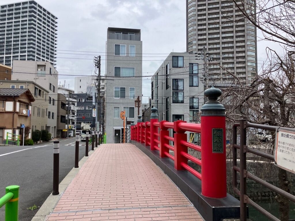 【春になったらロケ地】赤い欄干の橋とレンガの歩道高層ビルがそびえる日本の都市の街並み