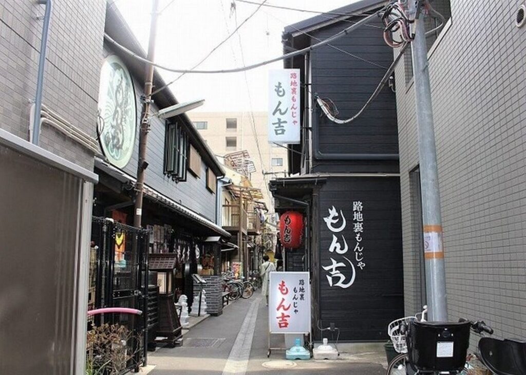 【春になったらロケ地】路地裏の黒い建物にもん吉もんじゃ焼き店が立ち並ぶ細い道
