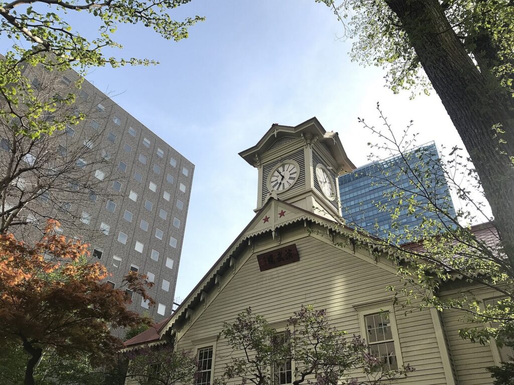 【日本三大がっかり名所】札幌時計台の白い建物が背景の高層ビルと木々に囲まれている様子