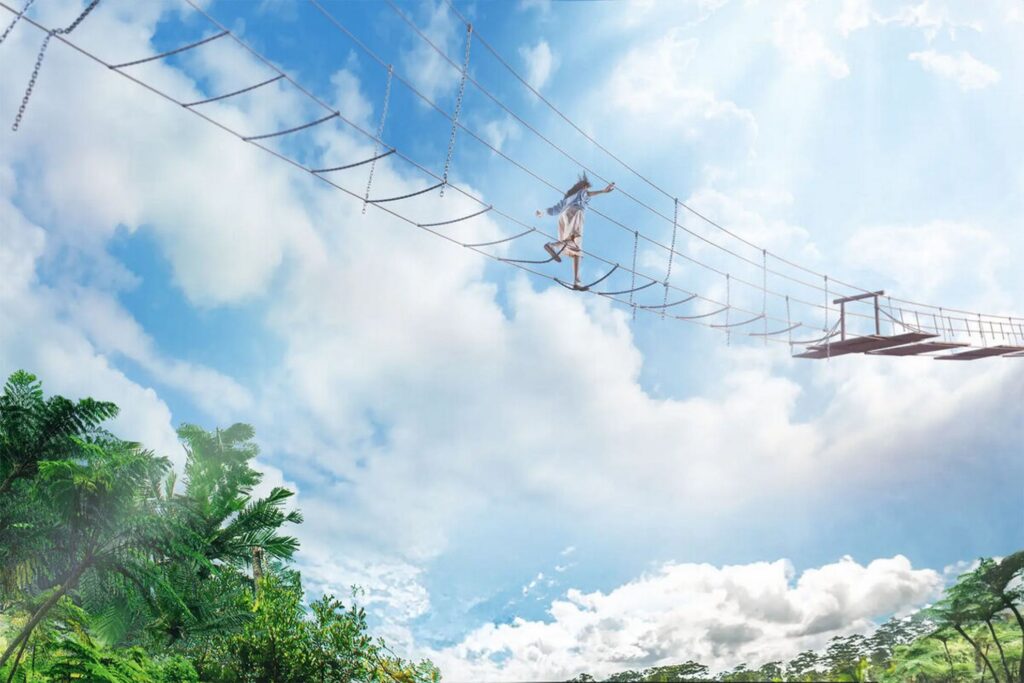 【ジャングリア沖縄 レビュー】青い空と雲の下で高い場所に架かるアスレチックの橋を女性がバランスを取りながら渡っている風景