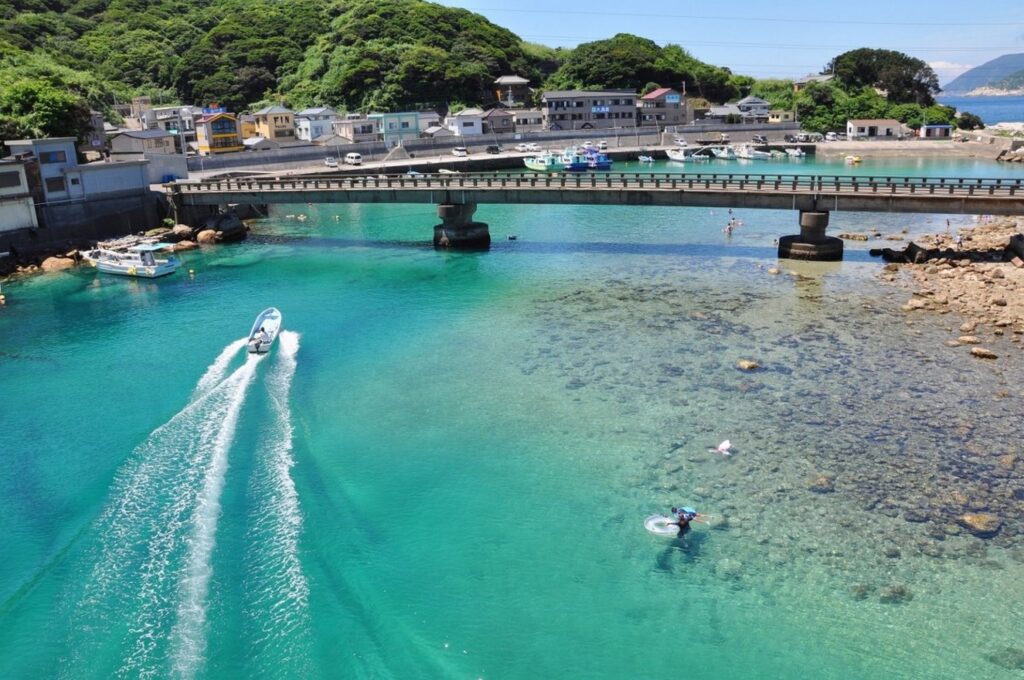 【柏島 がっかり】エメラルドグリーンの透き通った海を白い船が進み橋や家々が見える風景