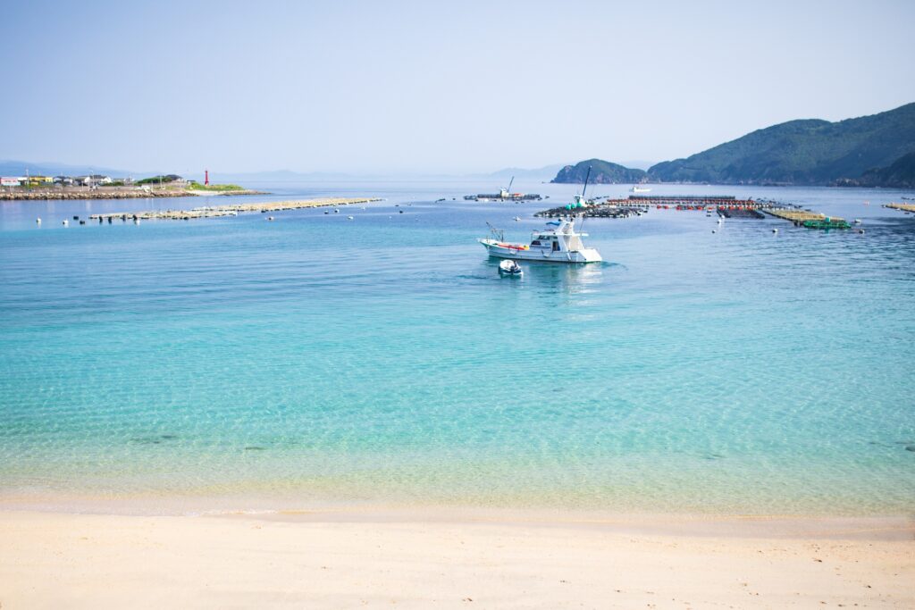 【柏島 がっかり】白い砂浜と透き通るエメラルドグリーンの海に白い船と養殖いかだが浮かぶ景色
