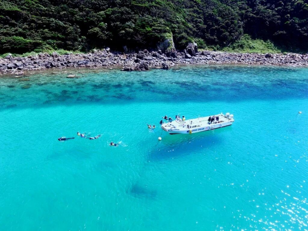 【柏島 がっかり】透明なエメラルドグリーンの海でシュノーケリングを楽しむ人々が白い船の周りを泳ぐ柏島の風景