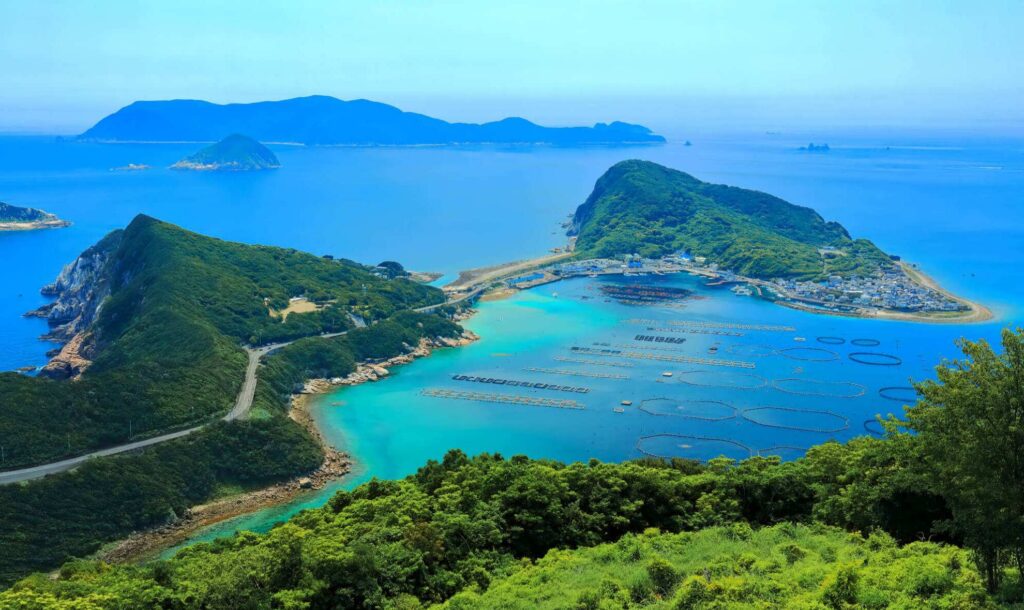 【柏島 がっかり】高台から見た青とエメラルドグリーンの海に細い道でつながる緑豊かな島と養殖いかだがある風景