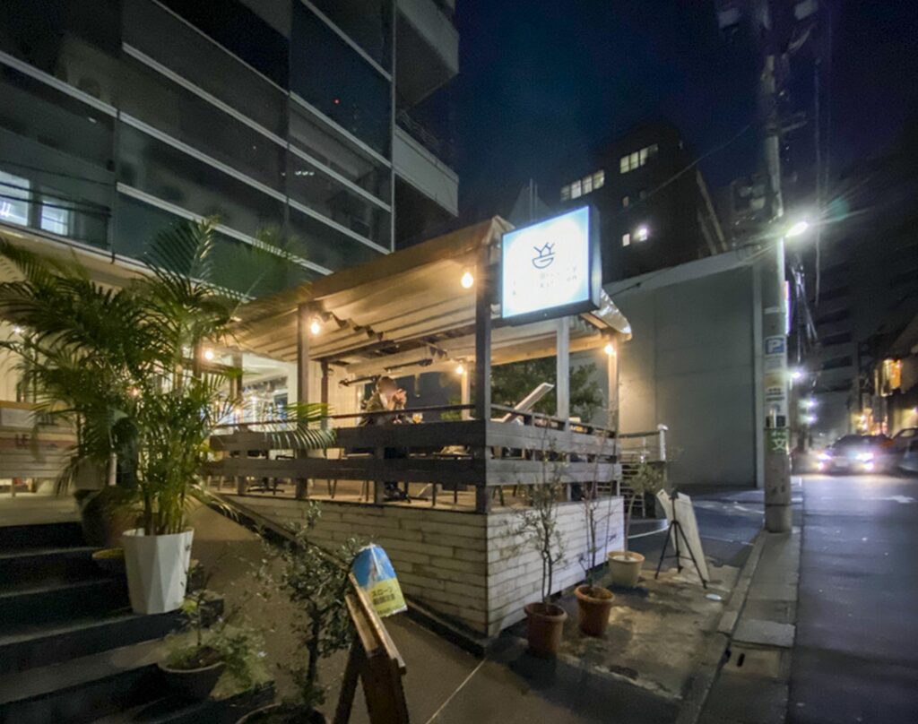 【けものになれない私たちロケ地】夜の街角にあるお店の温かい電球が灯るウッドテラスの外観