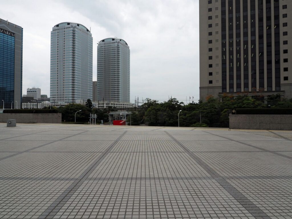 【歩道橋 ロケ地】灰色のタイルが敷き詰められた広い広場と並ぶ高層ビル群の都市風景