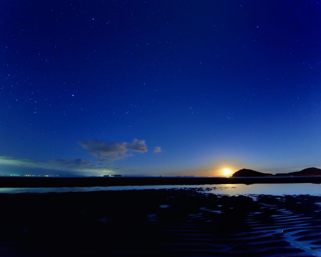 【Chichibugahama Beach】Night view of a beach with many stars in the sky and a bright moon reflecting on the water