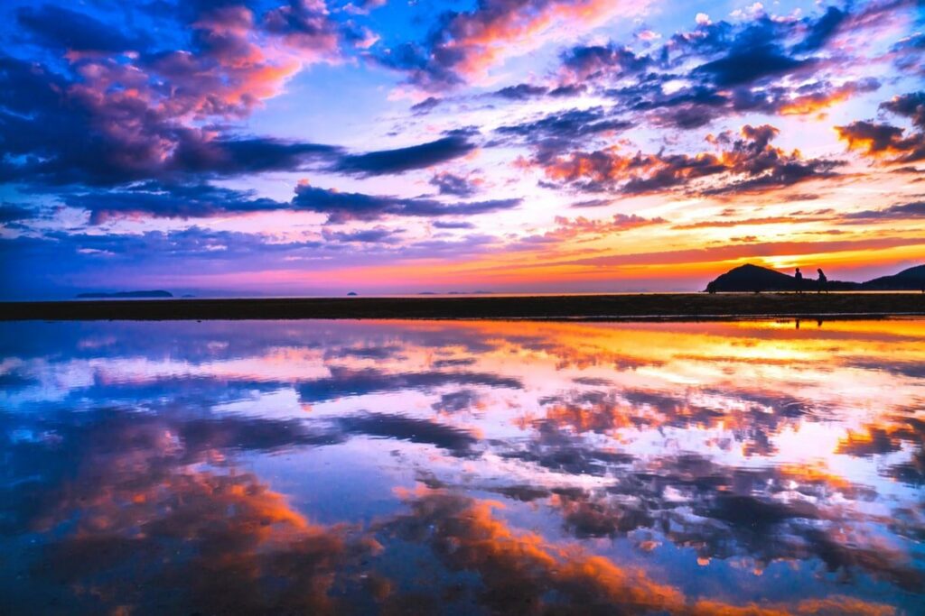 【Chichibugahama Beach】A vibrant sunset over a tidal flat with people silhouetted against the colorful sky and reflections in the wet sand.