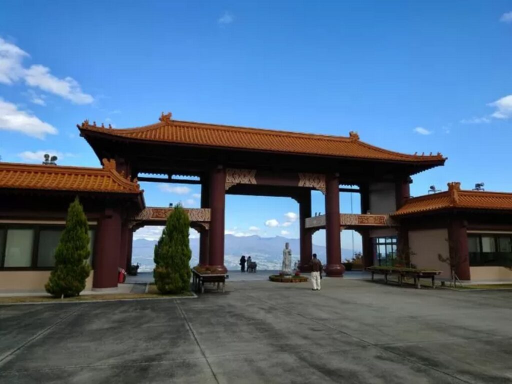【法水寺キングダムロケ地】赤い屋根の門と青空、背景に山が広がる風景