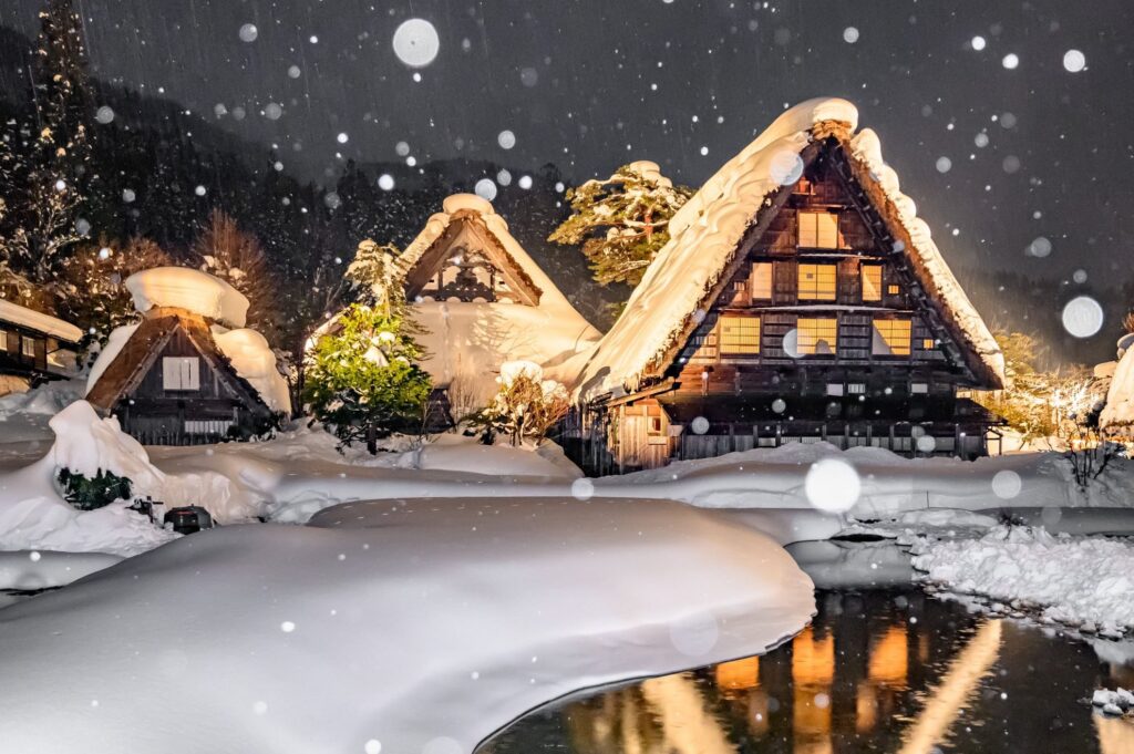 【Shirakawa-go】Gassho-zukuri houses covered in deep snow at night with falling snow and lights reflecting in the water